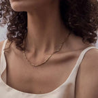 Close-up of a person wearing a gold necklace with a plain background