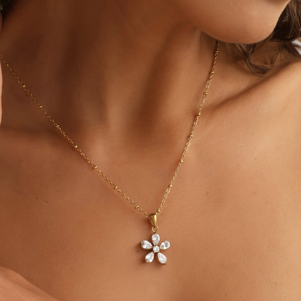 Gold necklace with a flower-shaped pendant worn by a person