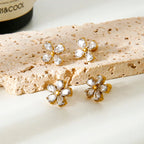 Gold flower-shaped earrings with clear stones on a textured beige surface.