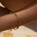 Gold bracelet with green gemstones on a person's wrist against a neutral background