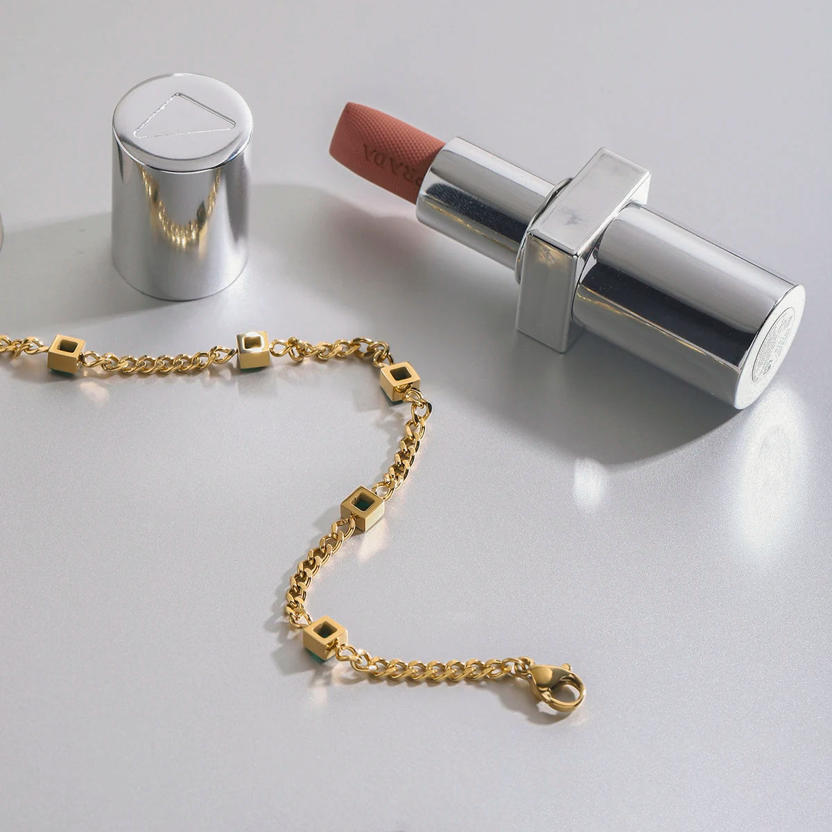 Gold bracelet and silver lipstick on a light gray background