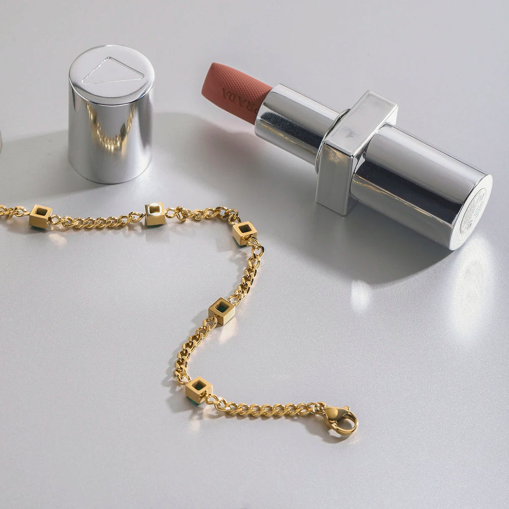 Gold bracelet and silver lipstick on a light gray background