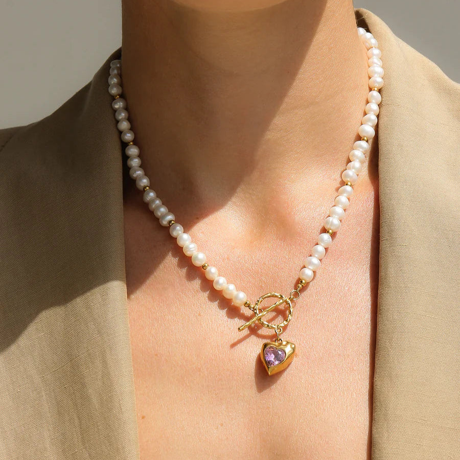 Close-up of a person wearing a pearl necklace with a heart-shaped pendant.