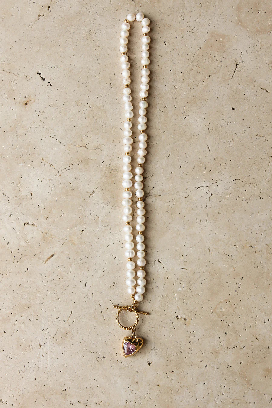 Pearl necklace with a heart-shaped pendant on a beige surface