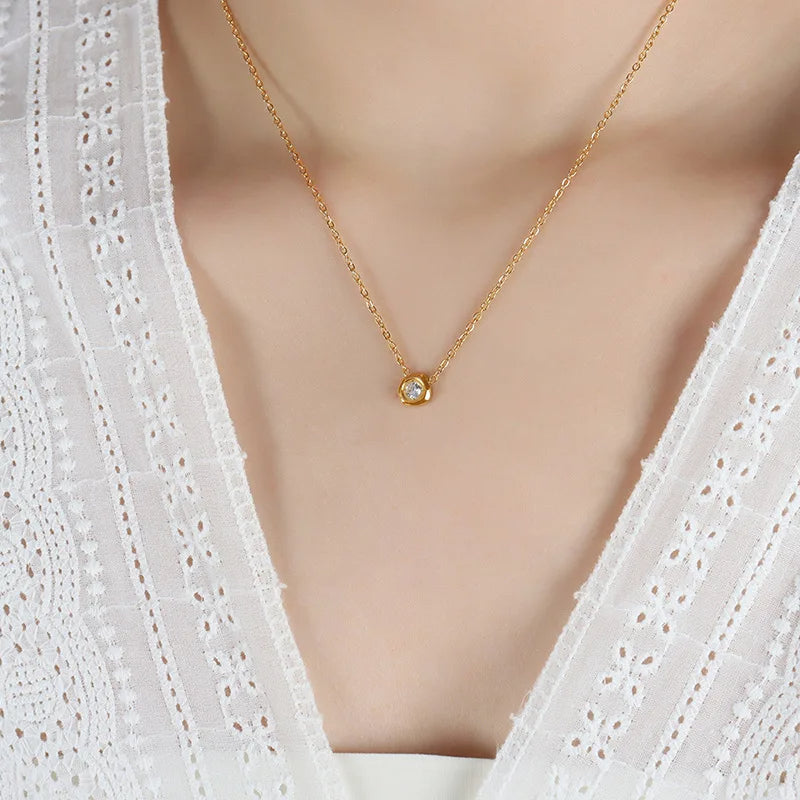 Gold necklace with a small pendant on a mannequin wearing a white lace top.