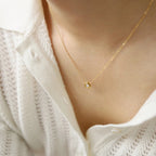 Gold necklace with a small pendant on a person wearing a white textured garment.