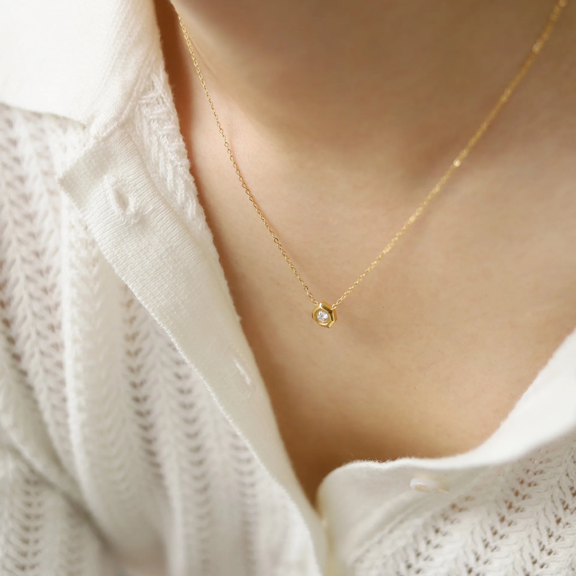 Gold necklace with a small pendant on a person wearing a white textured garment.