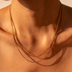 Close-up of a person wearing a gold chain necklace on a neutral background