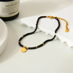 Black beaded bracelet with gold accents on a white surface next to a bottle labeled 'Capri & Co'.
