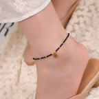 Ankle bracelet with black beads and a gold charm on a person's ankle.
