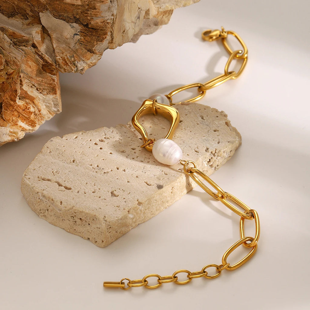 Gold chain necklace with a pearl pendant on a stone surface