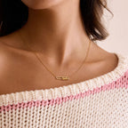 Necklace with a small pendant worn by a person wearing a pink and white patterned garment.