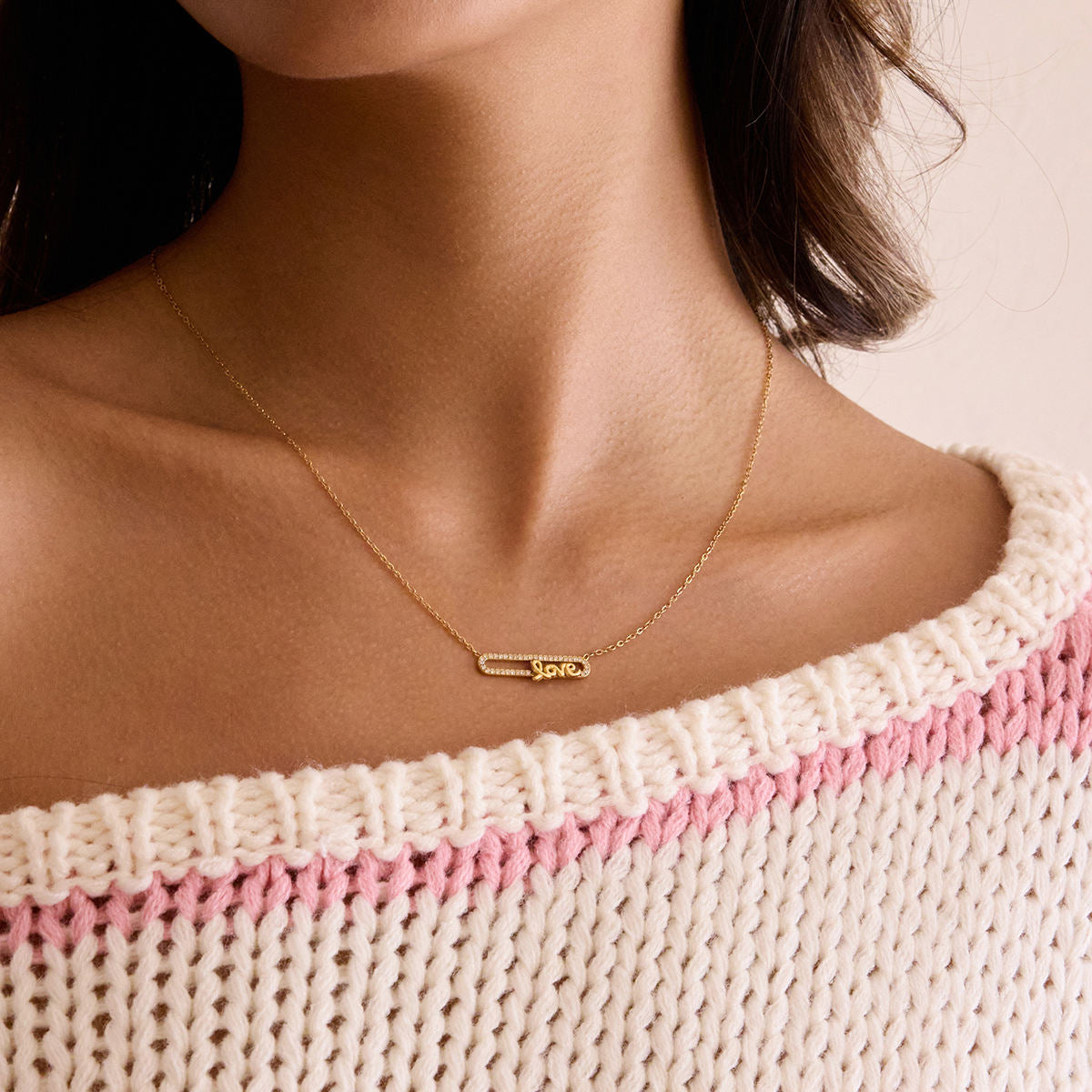 Necklace with a small pendant worn by a person wearing a pink and white patterned garment.