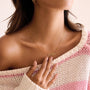 Woman wearing a gold necklace with a pendant, wearing a pink and white striped sweater.