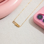 Gold necklace with 'love' pendant on a textured surface with pink phone case and pink object in the background