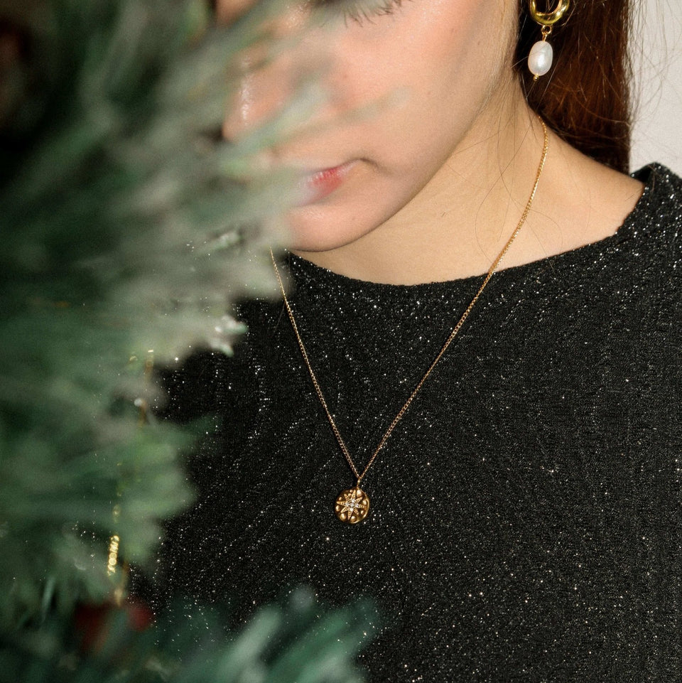 Person wearing a black glittery top and gold necklace with a green Christmas tree in the background