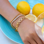 Hand wearing gold bracelets with lemons on a blue plate