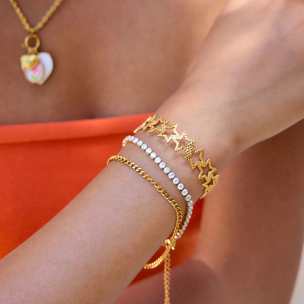 Close-up of a wrist wearing multiple gold bracelets with a bright orange background