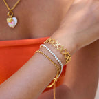 Close-up of a wrist wearing multiple gold bracelets with a bright orange background