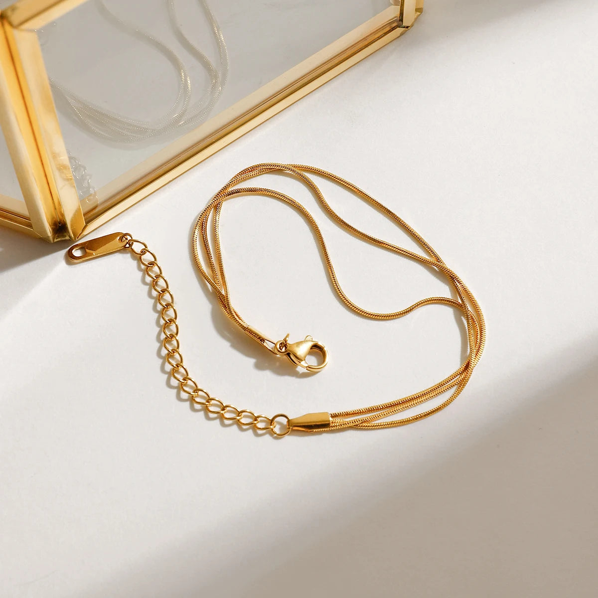 Gold bracelet and necklace on a white surface with a gold box in the background