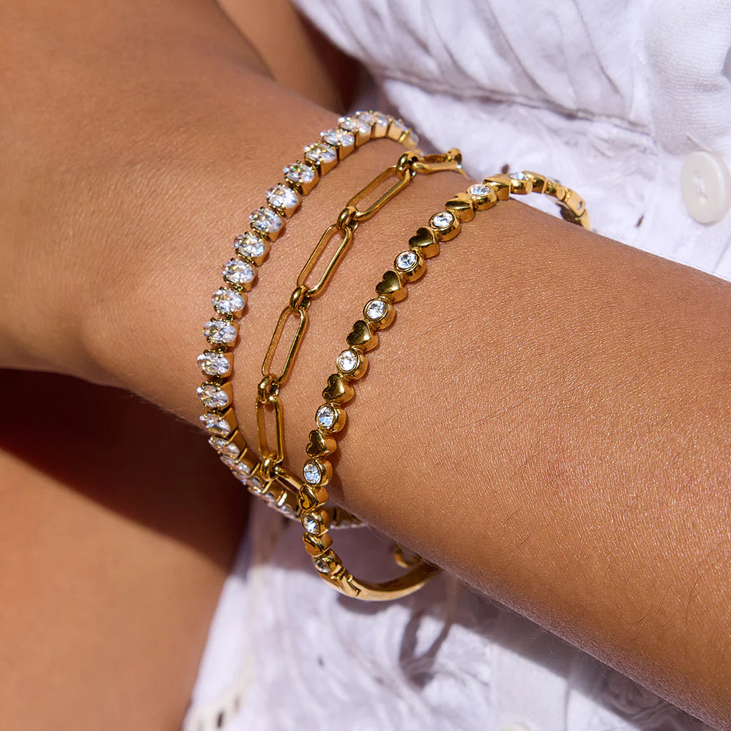 Gold bracelets with clear stones on a wrist against a neutral background