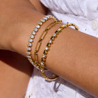 Gold bracelets with clear stones on a wrist against a neutral background