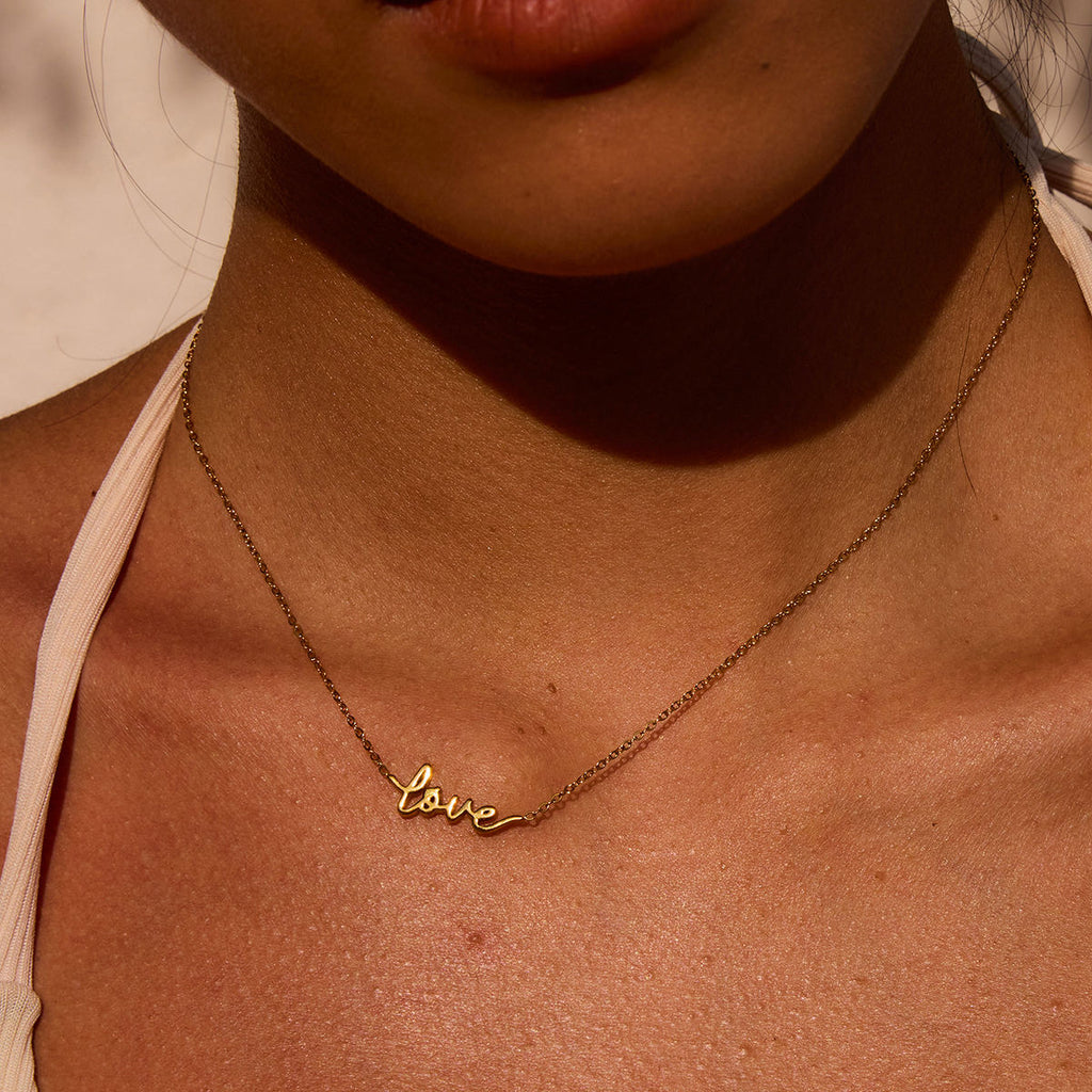 Gold 'love' necklace on a person's neck with a neutral background