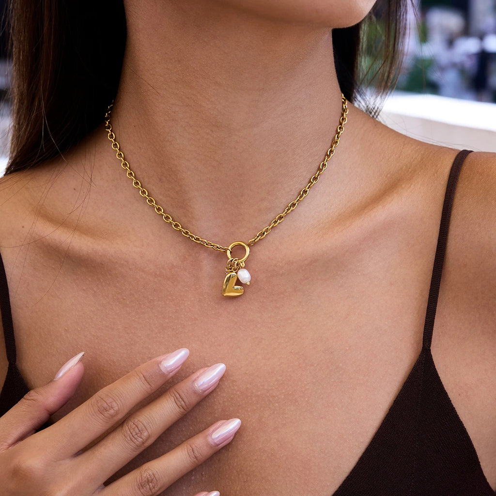 Gold necklace with heart and pearl charm worn by a person