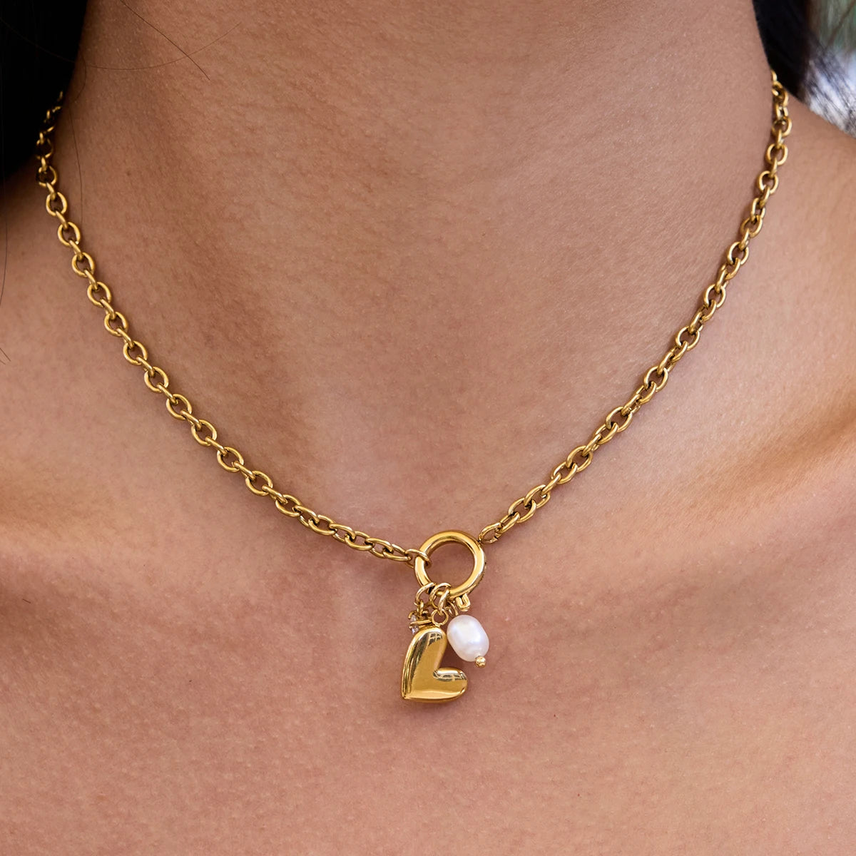 Gold necklace with a letter 'L' and pearl charm on a person's neck.