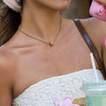 Close-up of a person wearing a gold necklace with a small pendant, holding a drink with a straw.