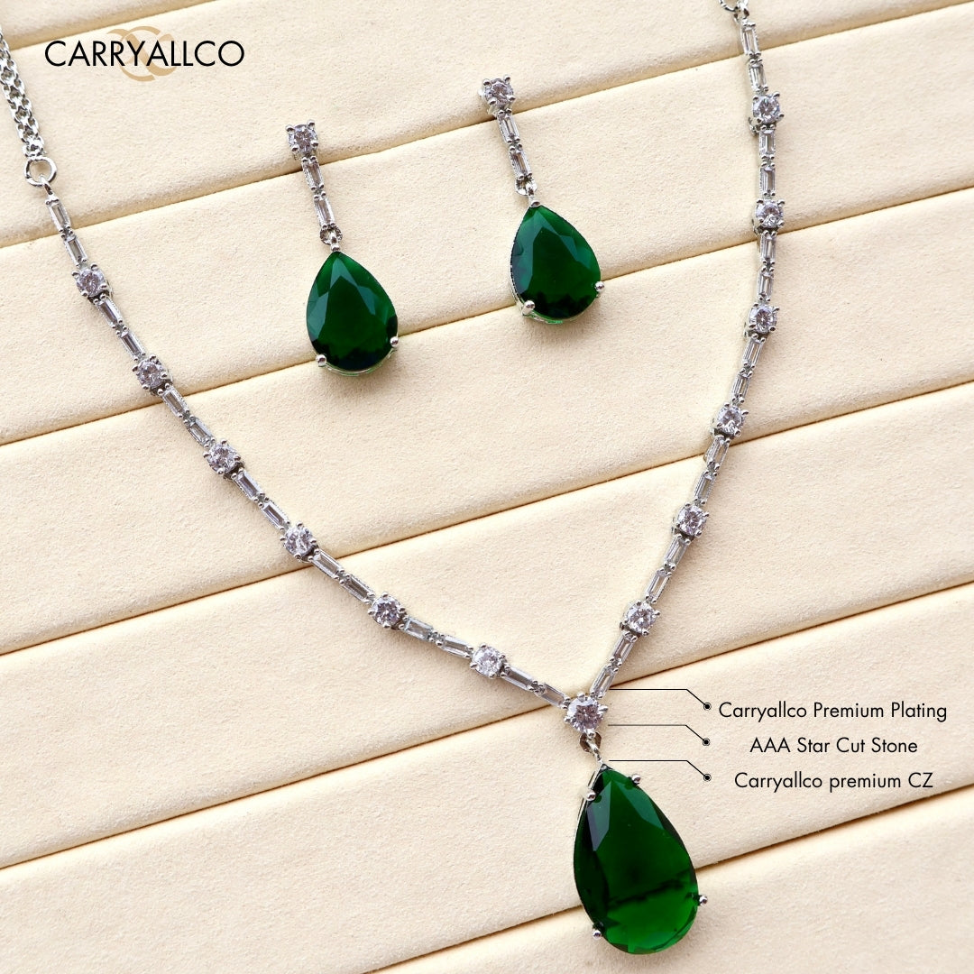 Jewelry set with green teardrop pendants and silver chain on a light wood background, featuring Carryalico branding.