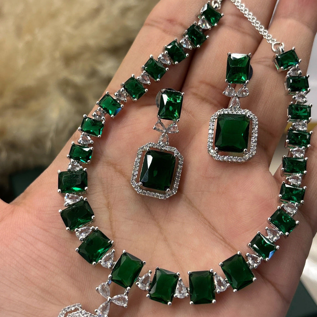 Emerald green gemstone necklace and earrings on a hand with a blurred background