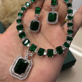 Green gemstone necklace and earrings held in a hand against a neutral background