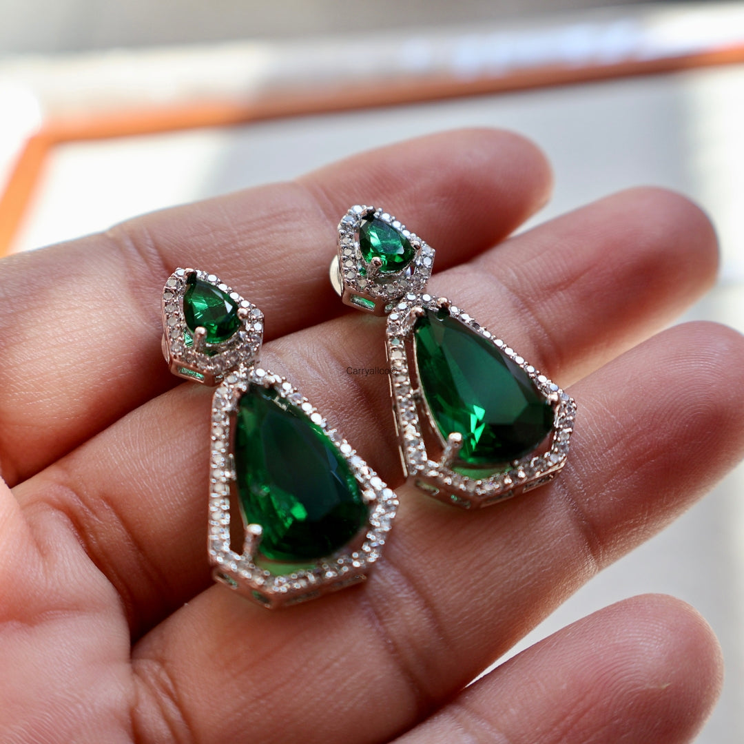 Green teardrop earrings held in a hand with a blurred background
