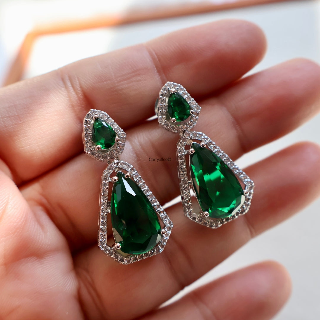 Green gemstone earrings held in a hand with a blurred background