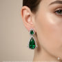 Close-up of a woman wearing a green teardrop earring with a beige background