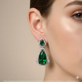 Close-up of a woman wearing a green teardrop earring with a beige background