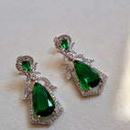 Pair of green teardrop earrings with silver accents on a light background