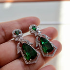 Green gemstone earrings held in a hand with a blurred background