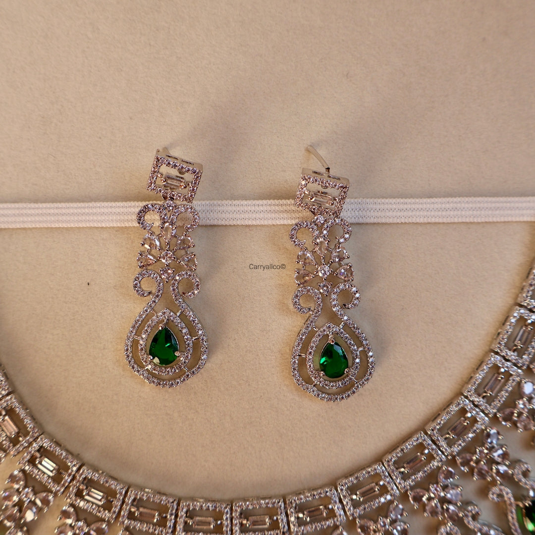 Pair of silver earrings with green gemstones on a beige background