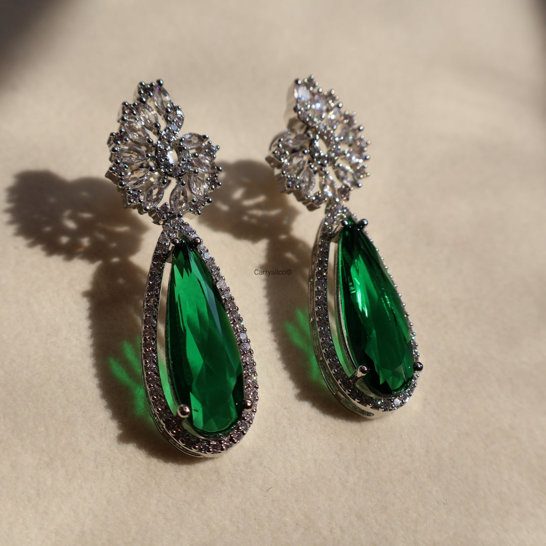 Pair of green teardrop earrings with silver and gemstone details on a beige background
