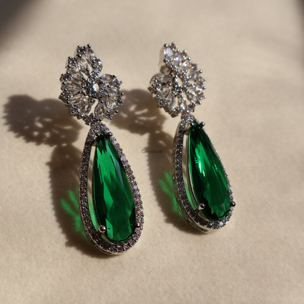 Pair of green teardrop earrings with silver and gemstone details on a beige background