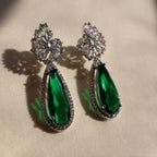 Pair of green teardrop earrings with silver and gemstone details on a beige background