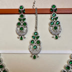 Green and silver earrings on a wooden stick against a beige background