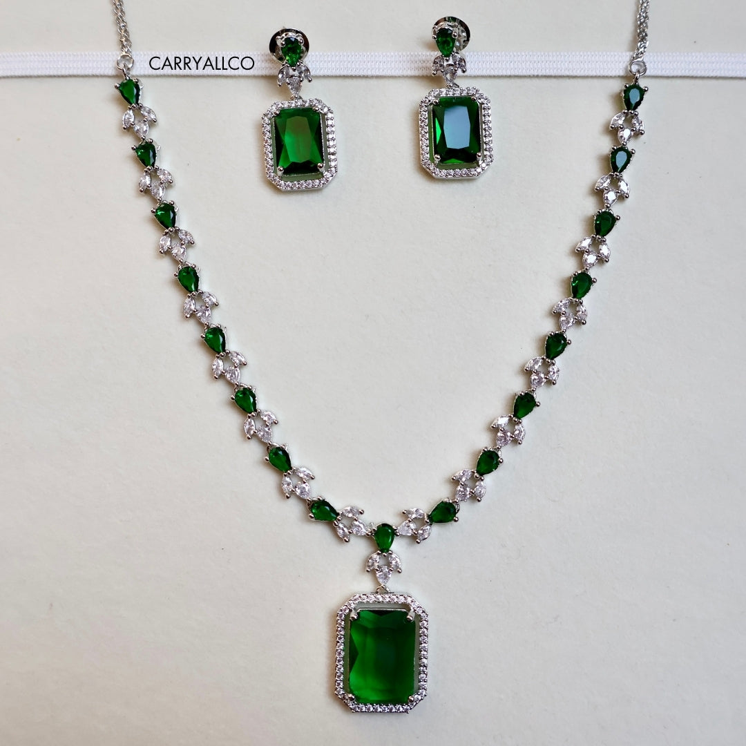 Jewelry set with necklace and earrings featuring green gemstones on a white background.