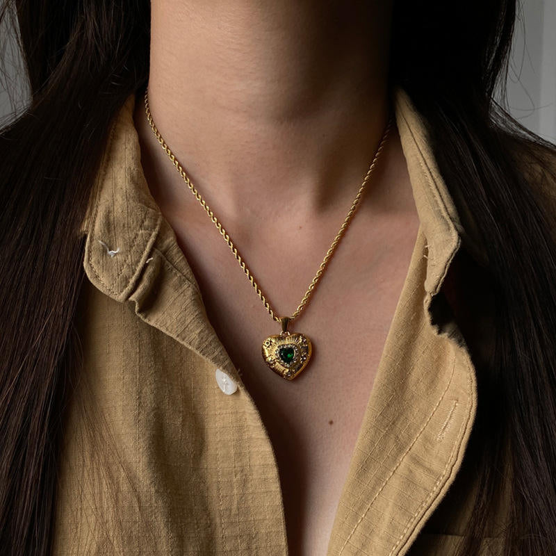 Gold necklace with a heart-shaped pendant worn by a person in a beige shirt.