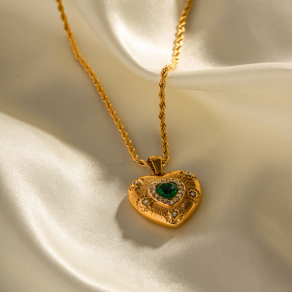 Gold heart-shaped pendant with a green gemstone on a beige fabric background