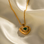 Gold heart-shaped pendant with a green gemstone on a beige fabric background