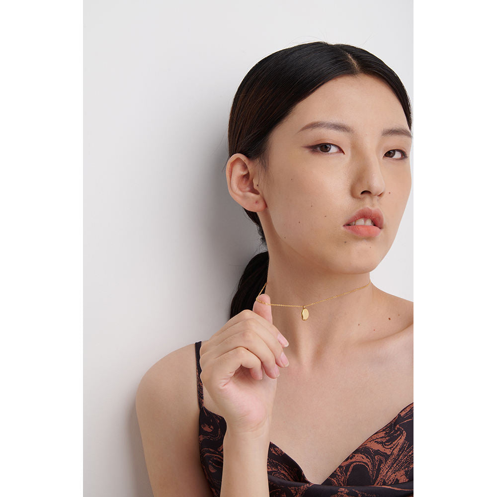 Woman wearing a gold necklace against a plain background