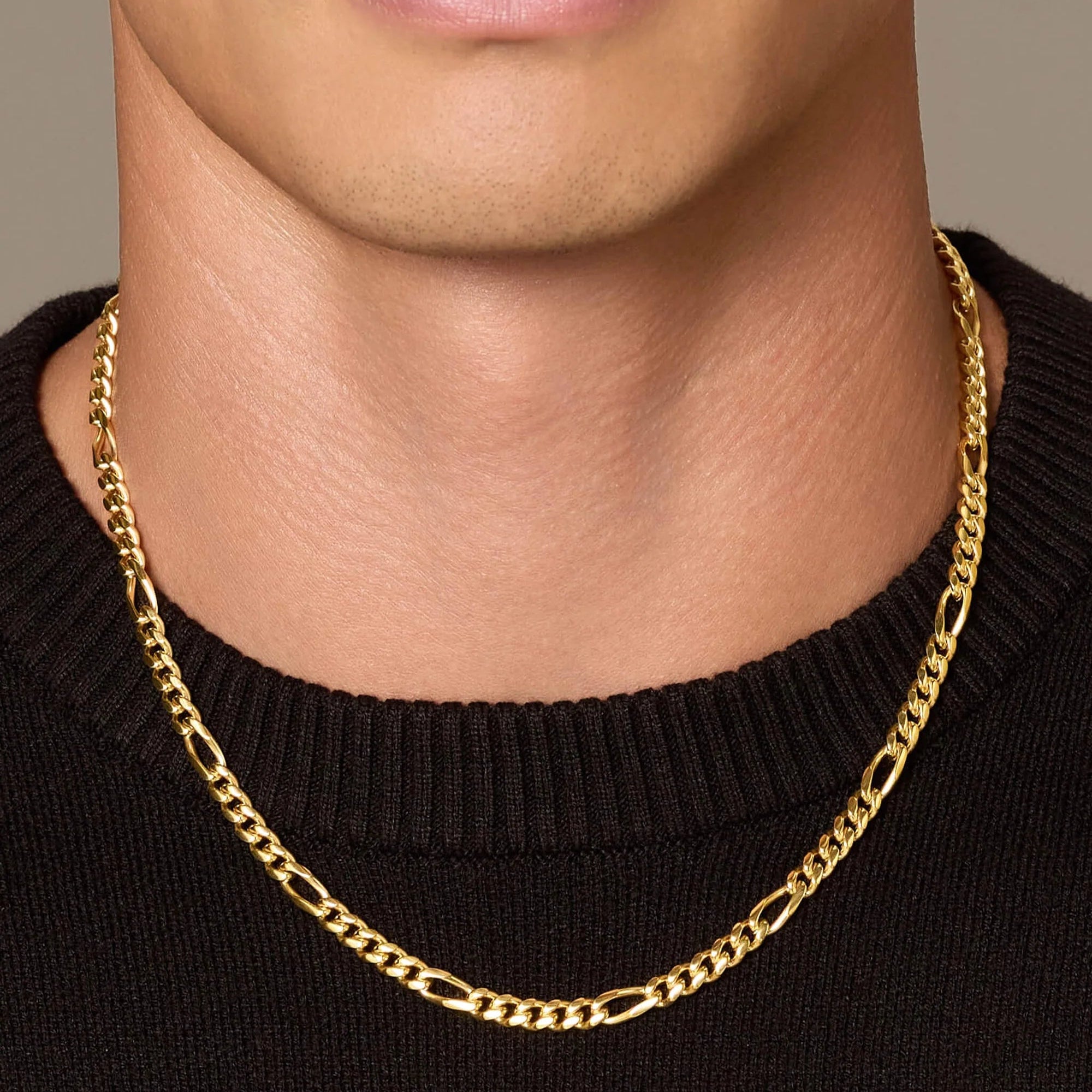 Gold chain necklace worn by a person against a neutral background